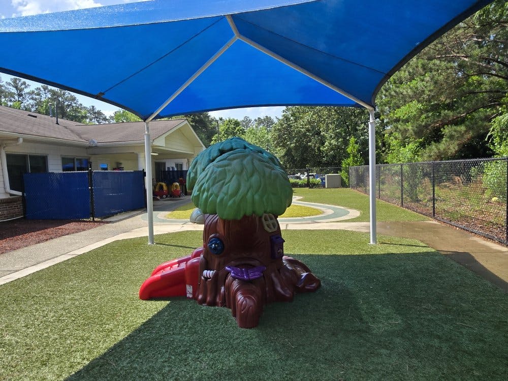 Playground with a tree stump slide and blue canopy over artificial turf