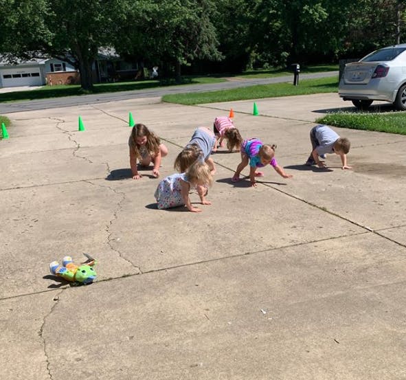 Children crawling on a paved surface with green cones