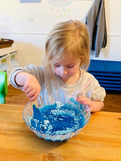 Child mixing blue slime with white beads in a clear bowl
