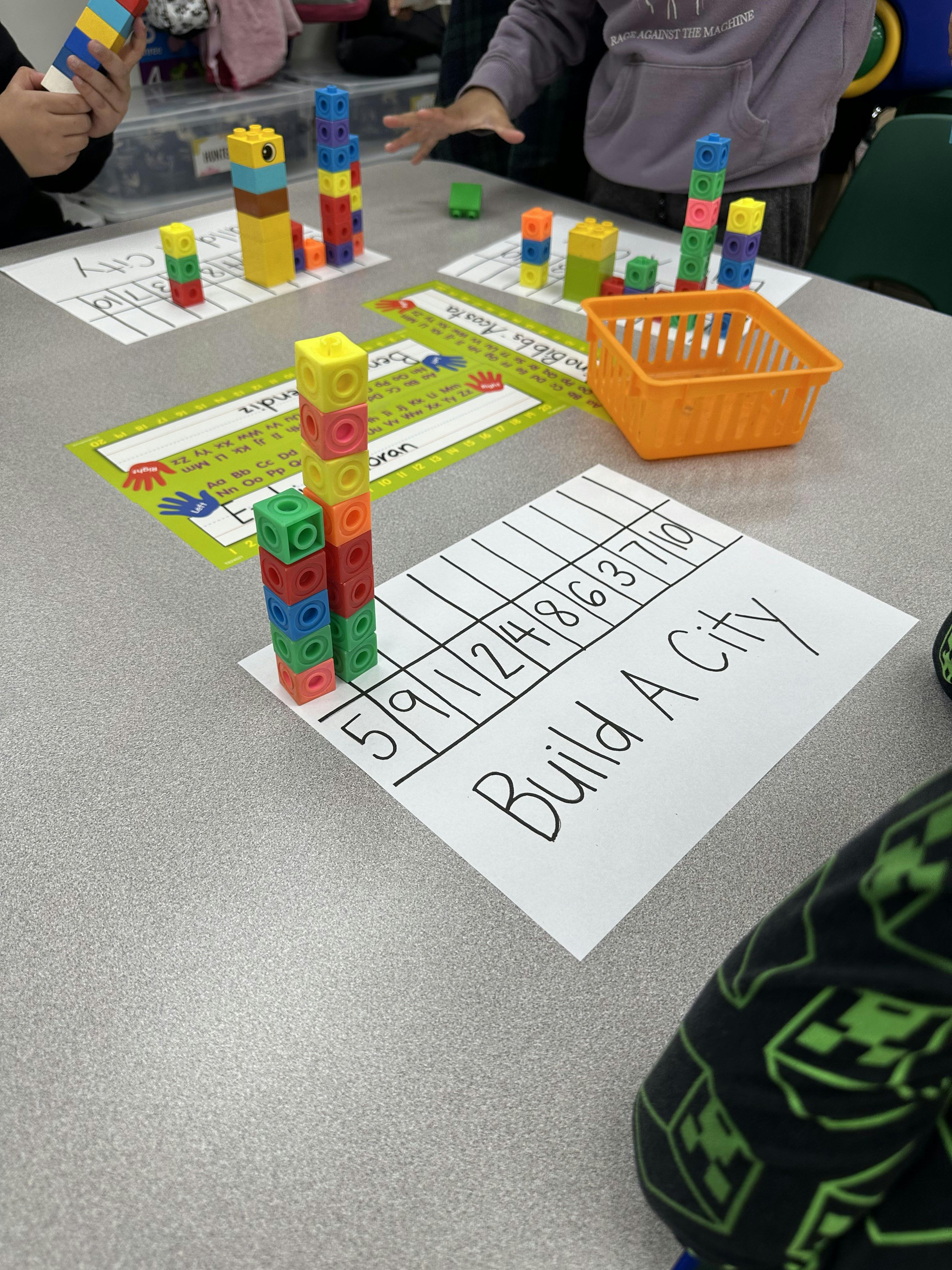 Children building with colorful interlocking blocks on a table with activity sheets