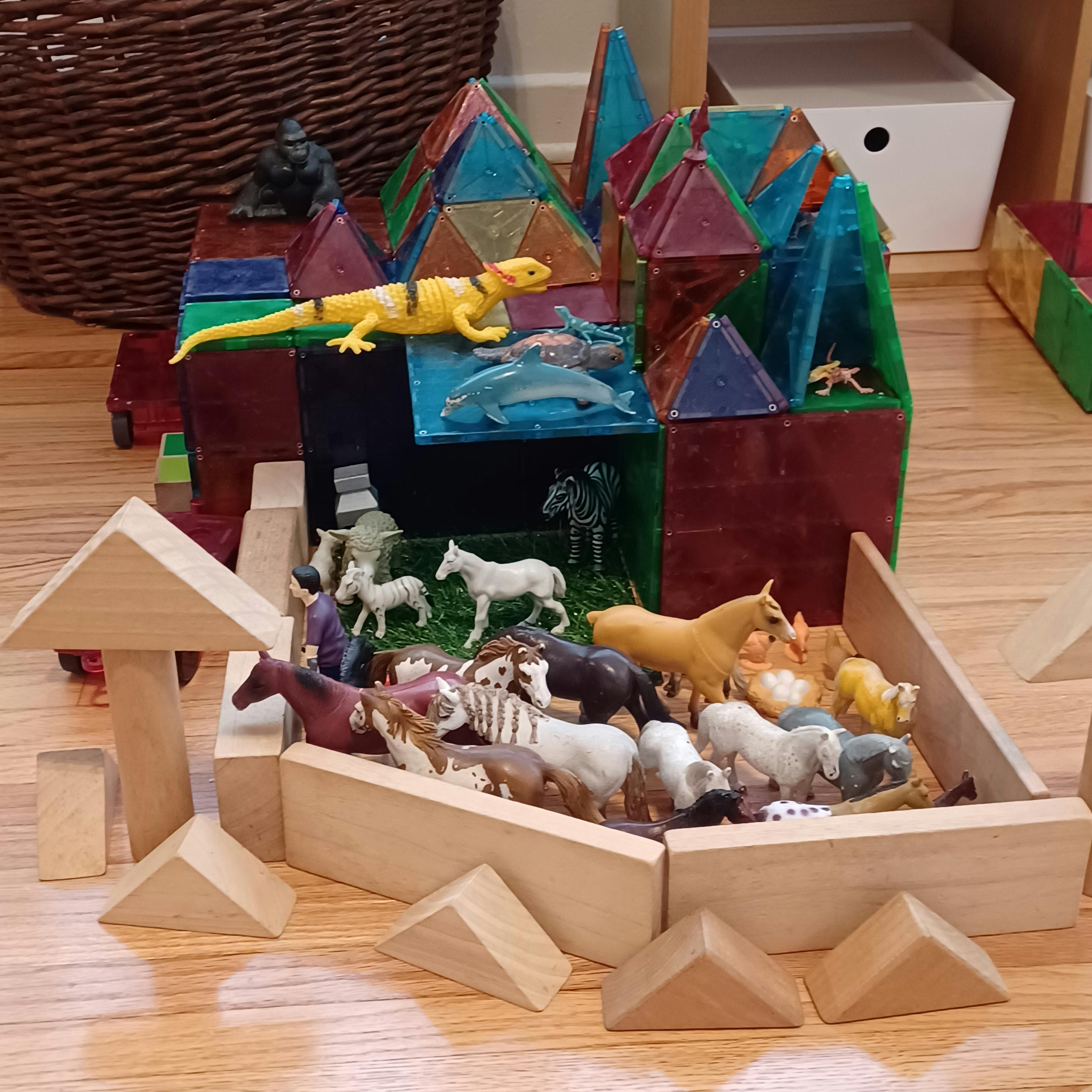 Toy animals in a wooden block enclosure next to magnetic tile structures
