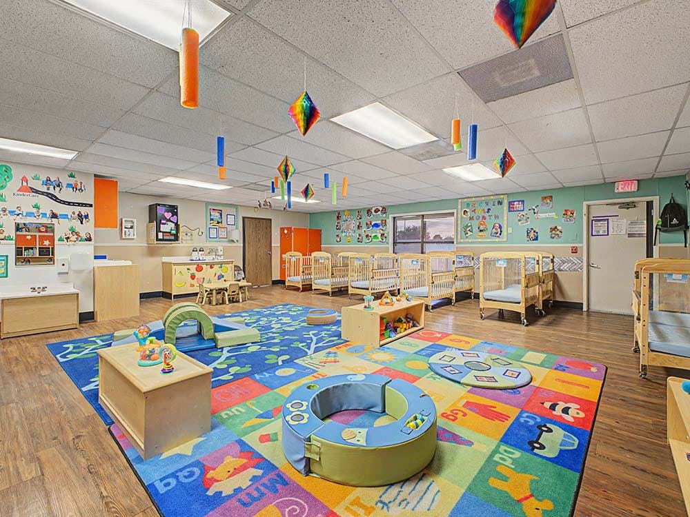 Colorful daycare classroom with cribs, playmats, and learning materials
