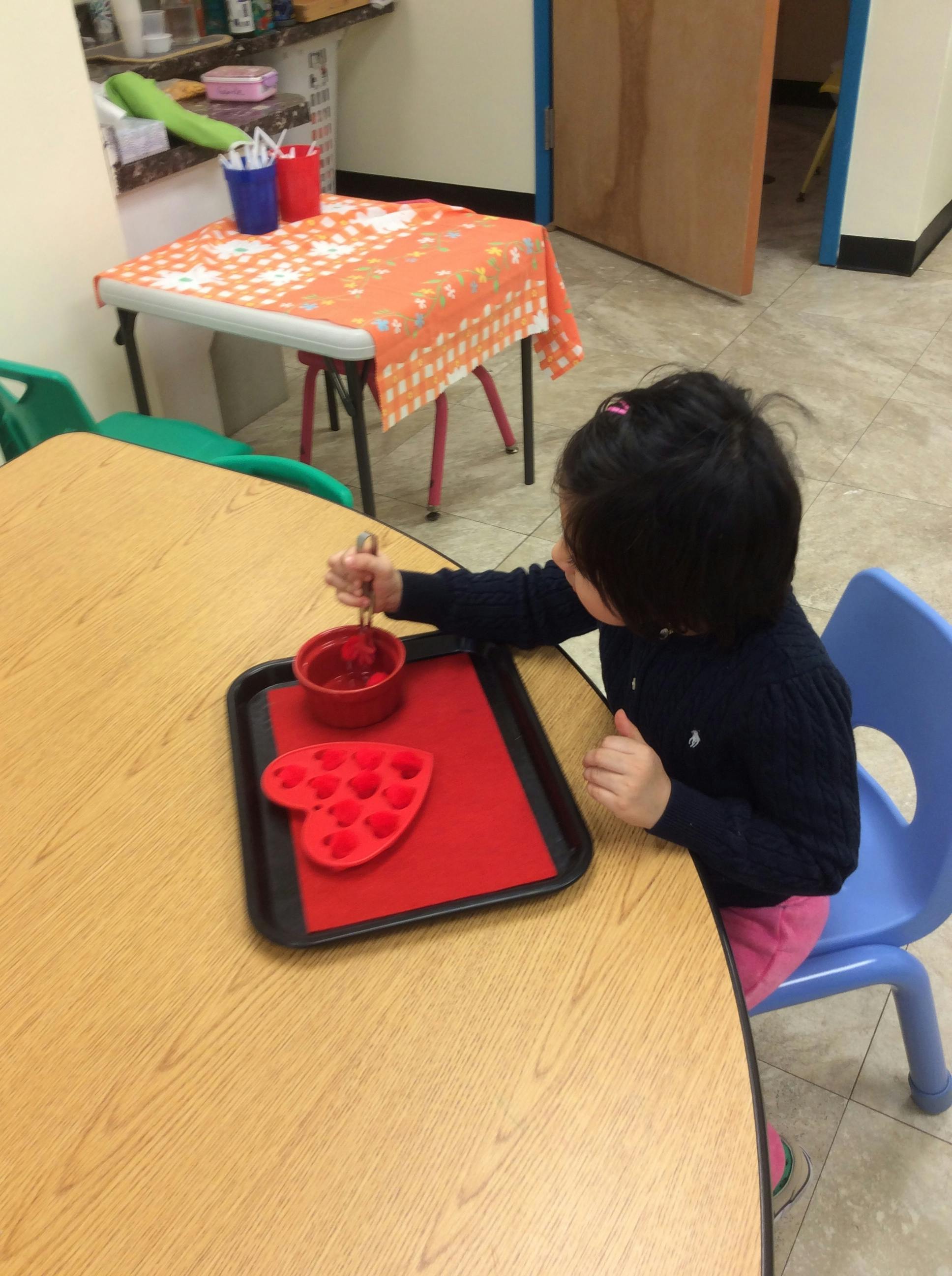 Child stirring contents in a red bowl on a tray with a heart-shaped mold