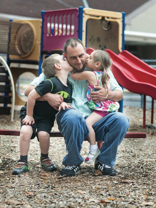 Person sitting with a child on each side kissing their cheeks