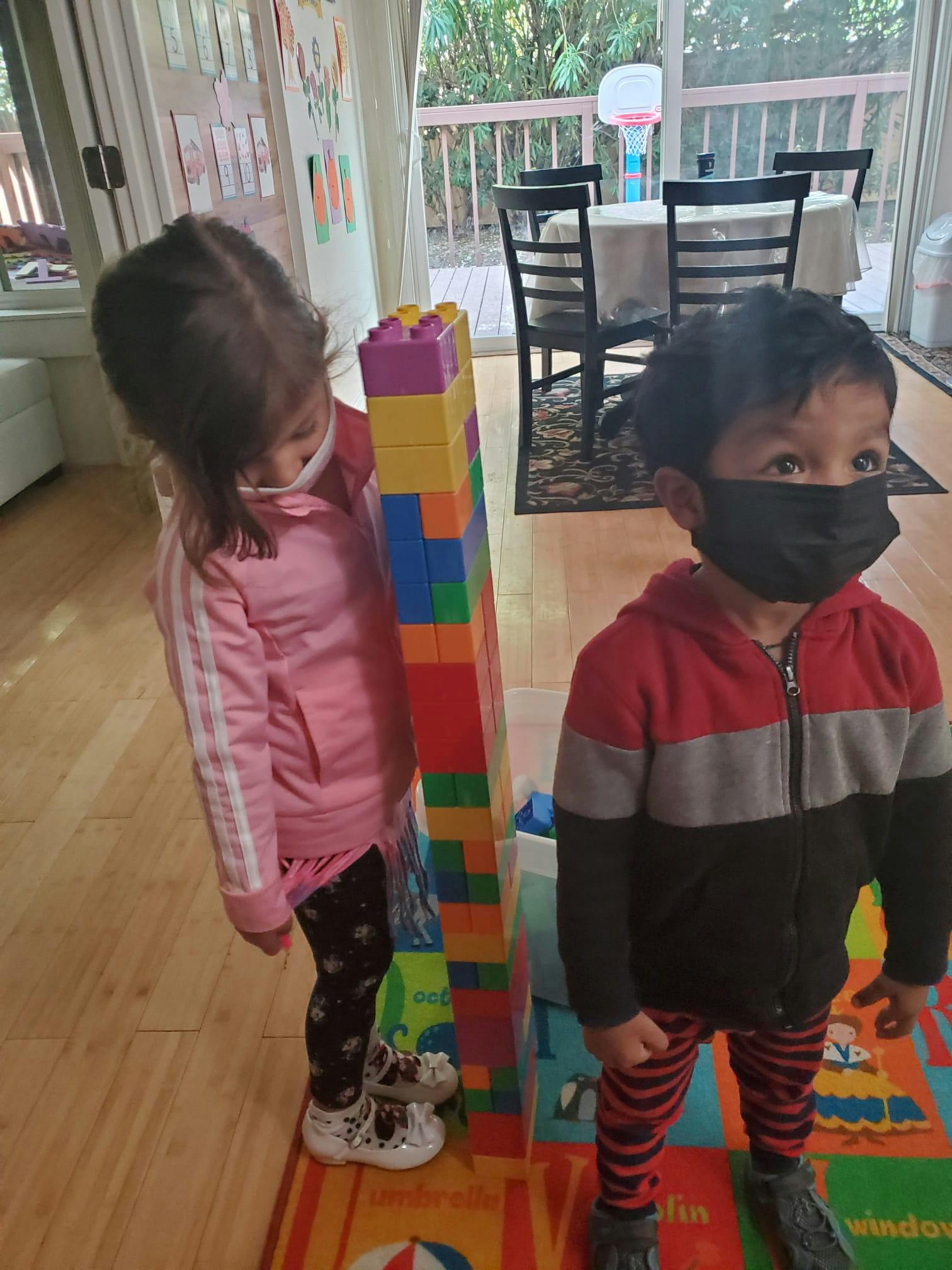 Two children standing next to a tall stack of colorful building blocks