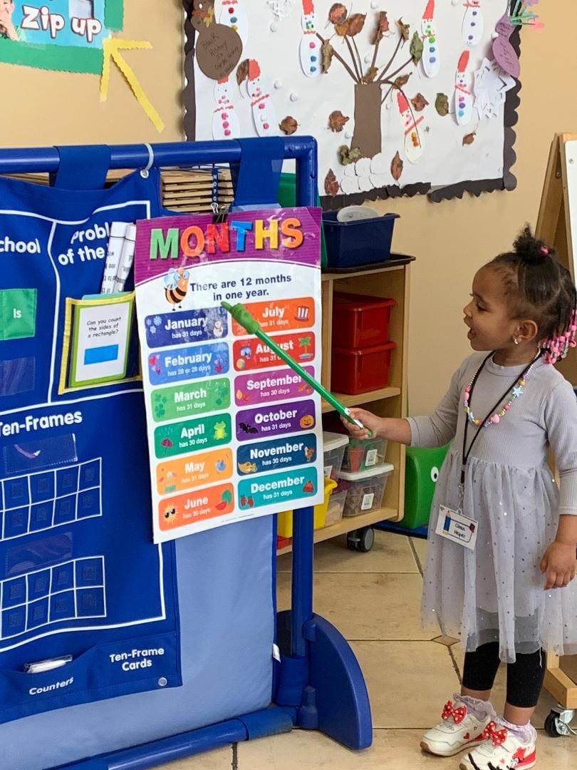 Child pointing to a "Months" chart in a classroom