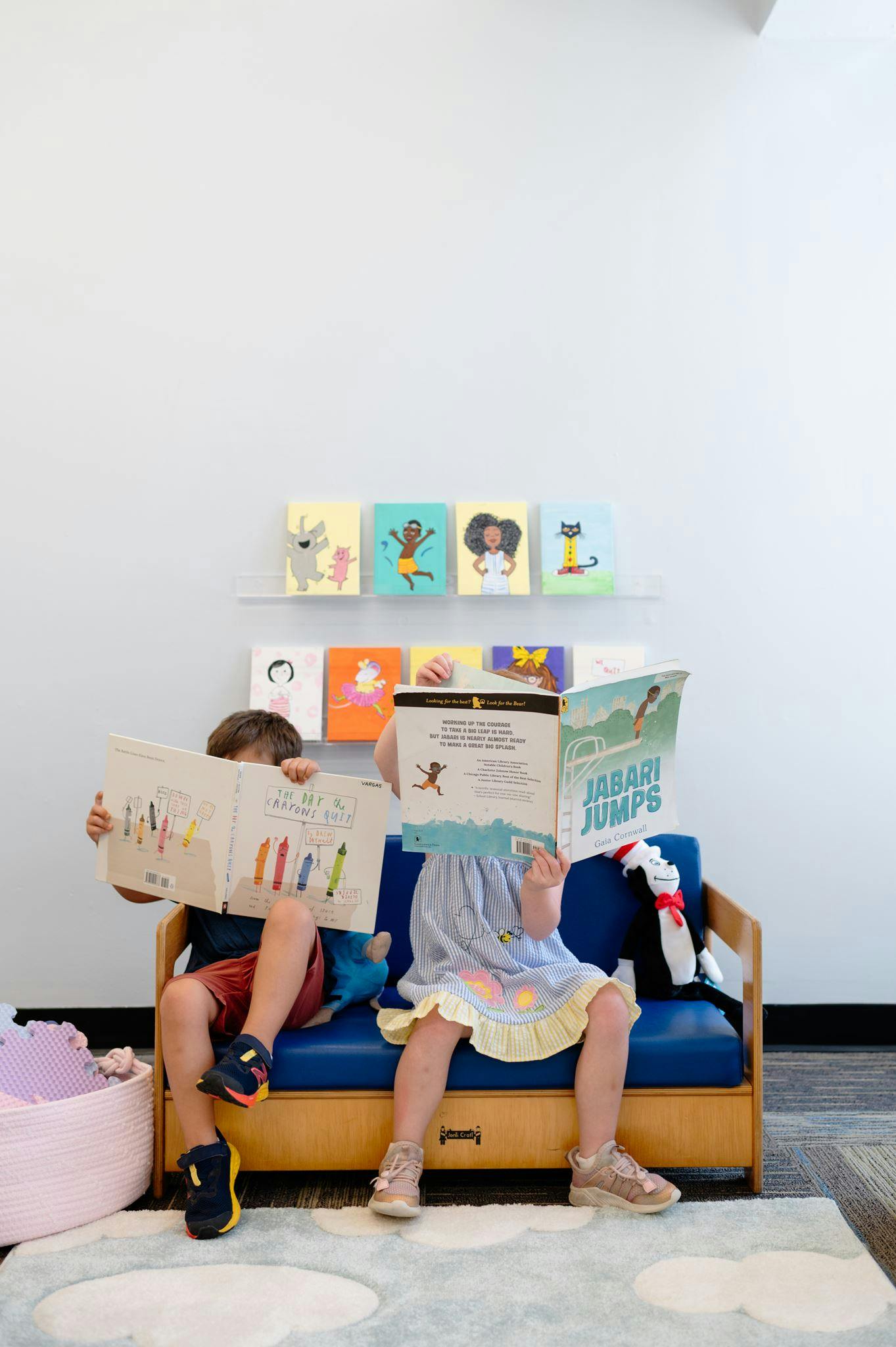 Two children sitting on a small blue bench reading picture books