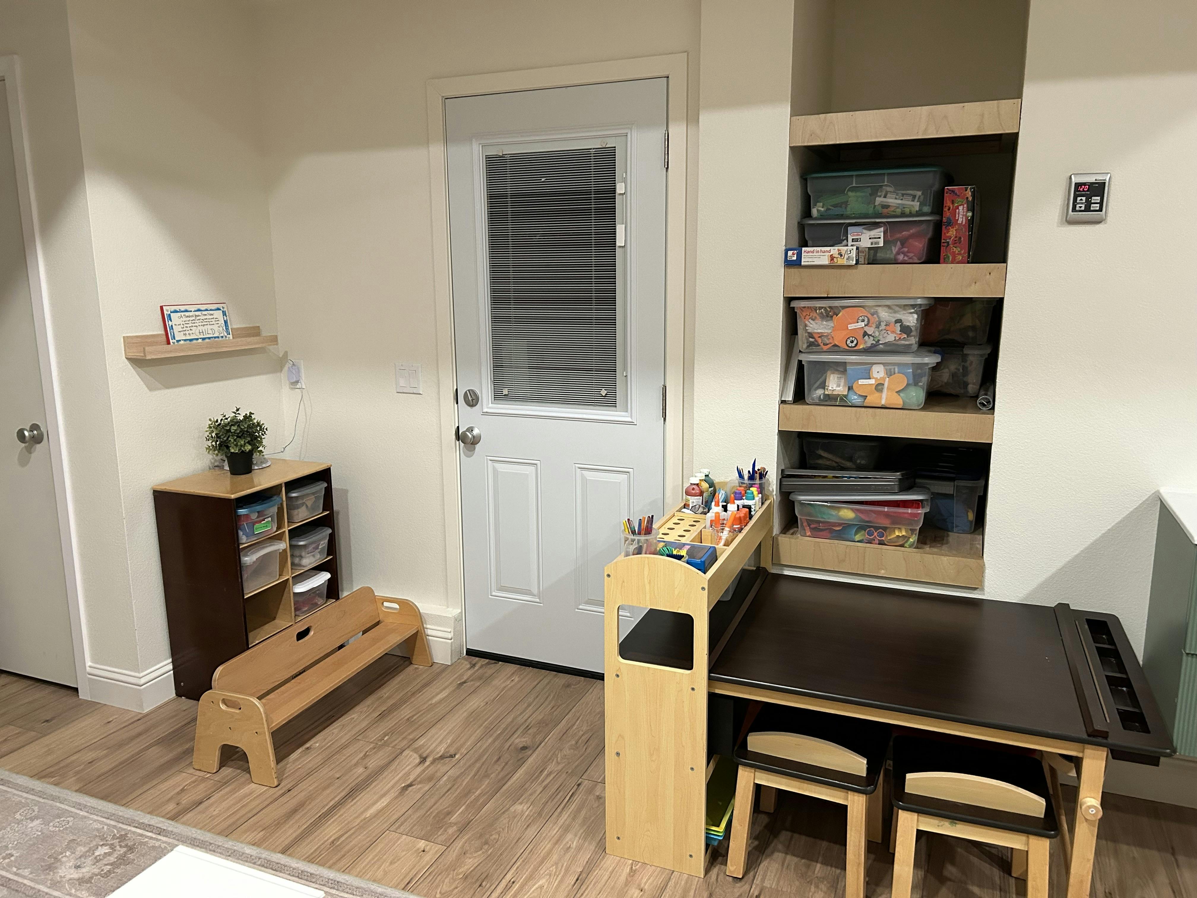 Children's play area with a small table and chairs, storage shelves, and a bench