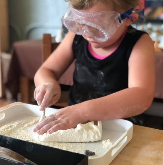 Child wearing safety goggles digging into a block of material
