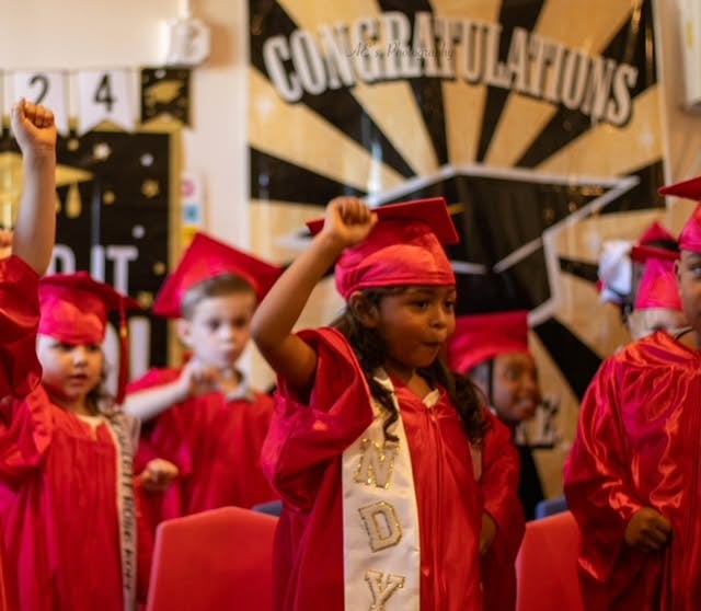Children wearing red graduation caps and gowns during a ceremony