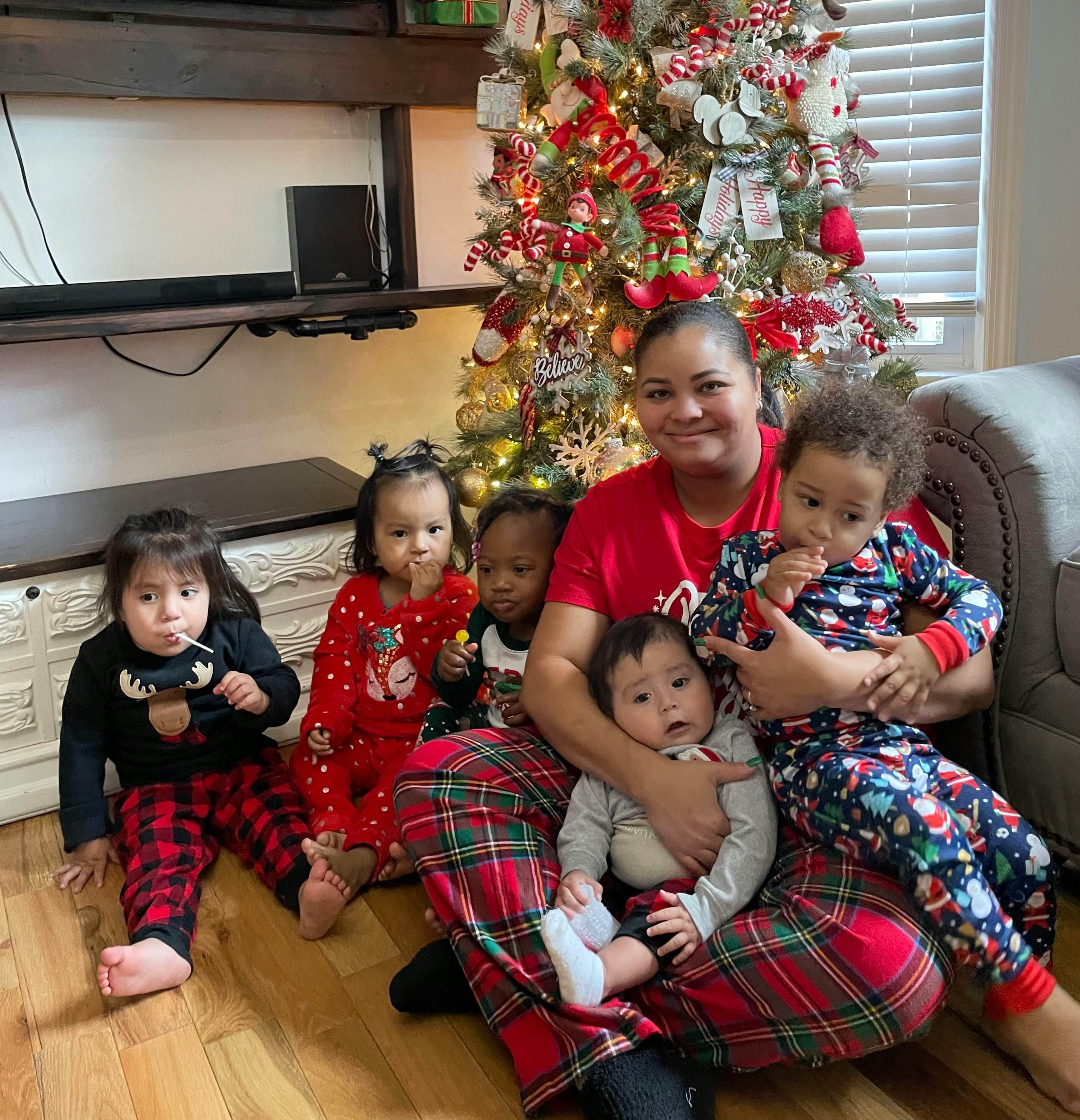 Person sitting on floor with five children in front of a Christmas tree