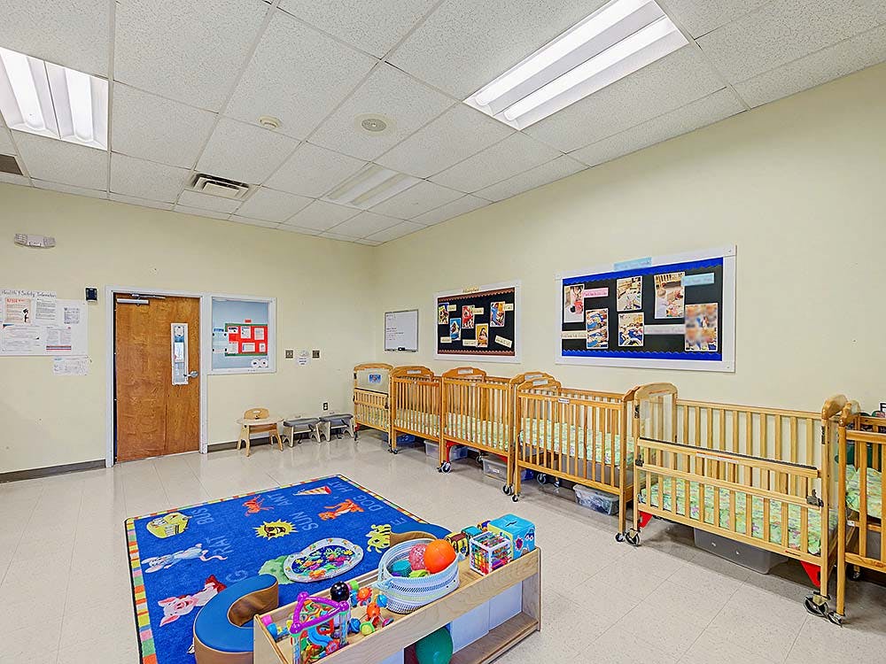 Cribs inside a daycare room with a playmat and toys on the floor