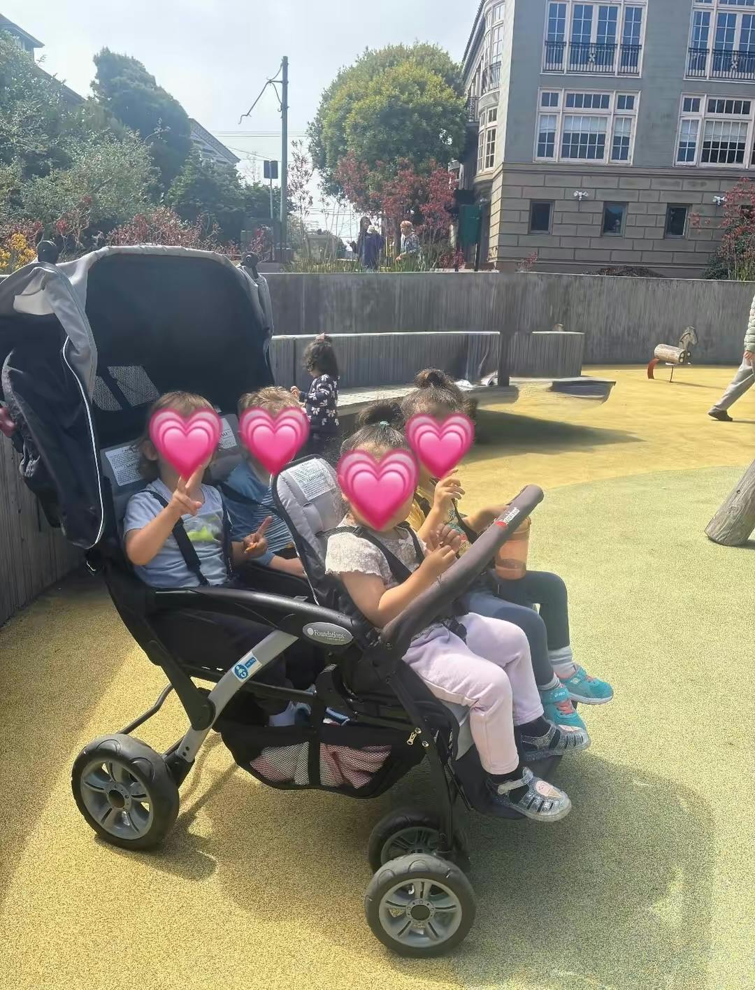 Four children sitting in a multi-seat stroller at a playground