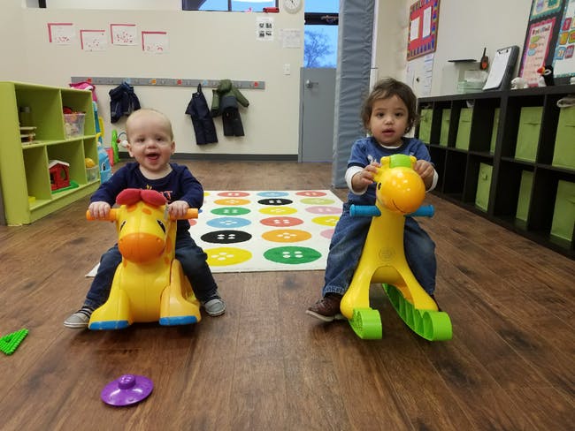 Two children riding toy giraffes on a wooden floor