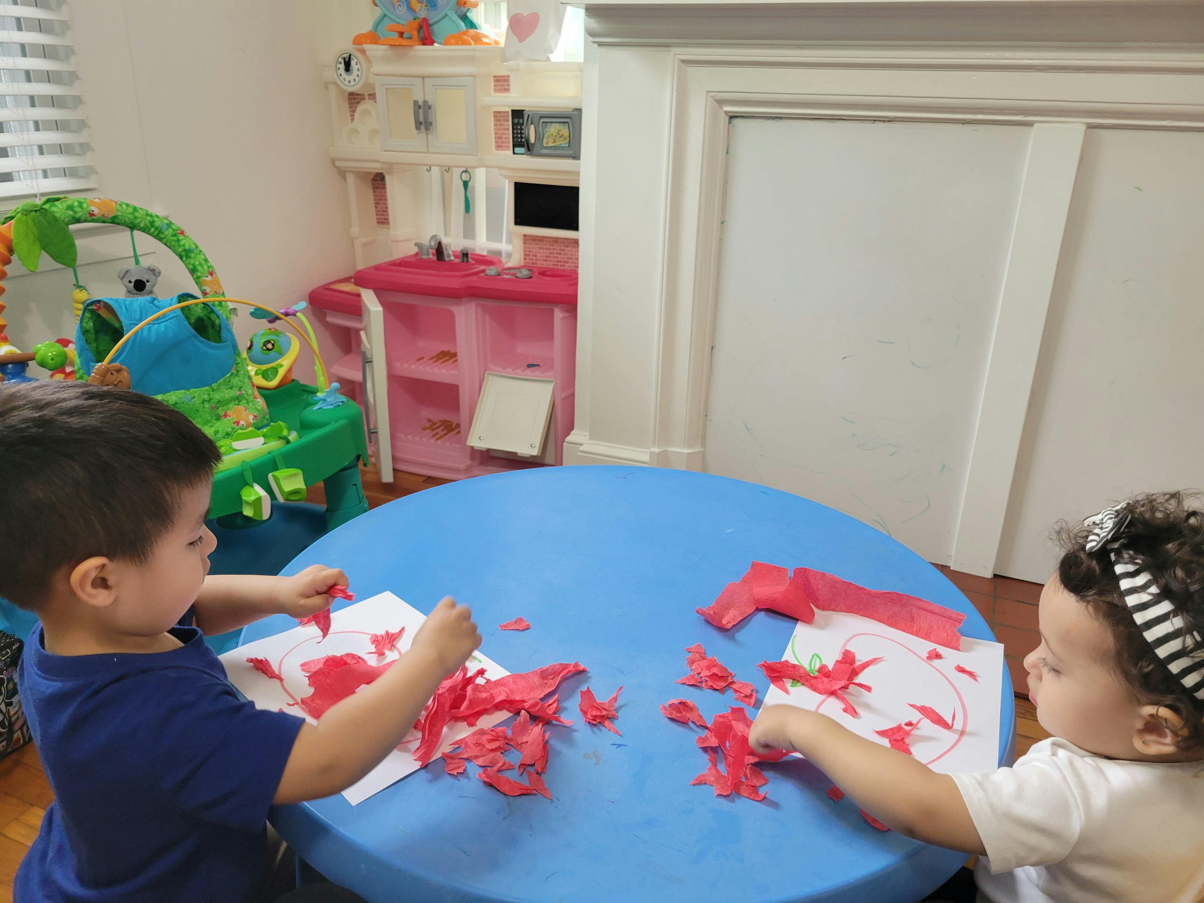 Two children at a table playing with red paper