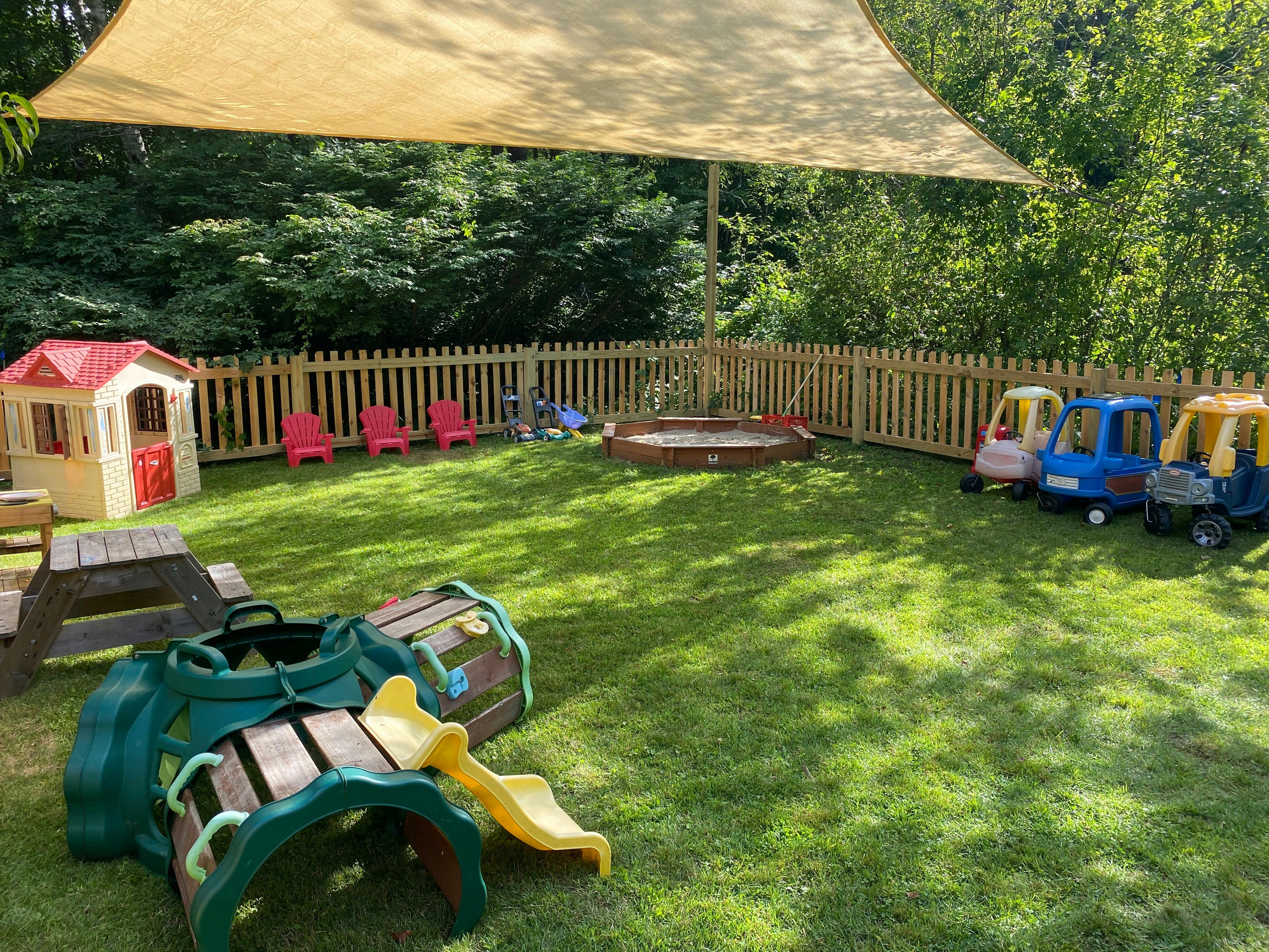 Outdoor play area with a small playhouse, sandbox, and toy cars