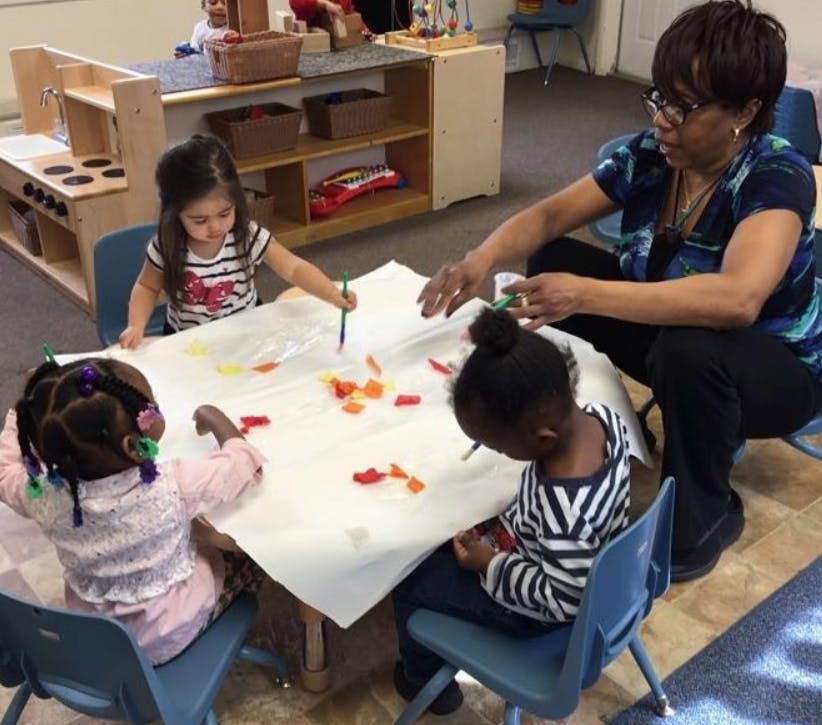 Adult and three children painting at a table in a classroom