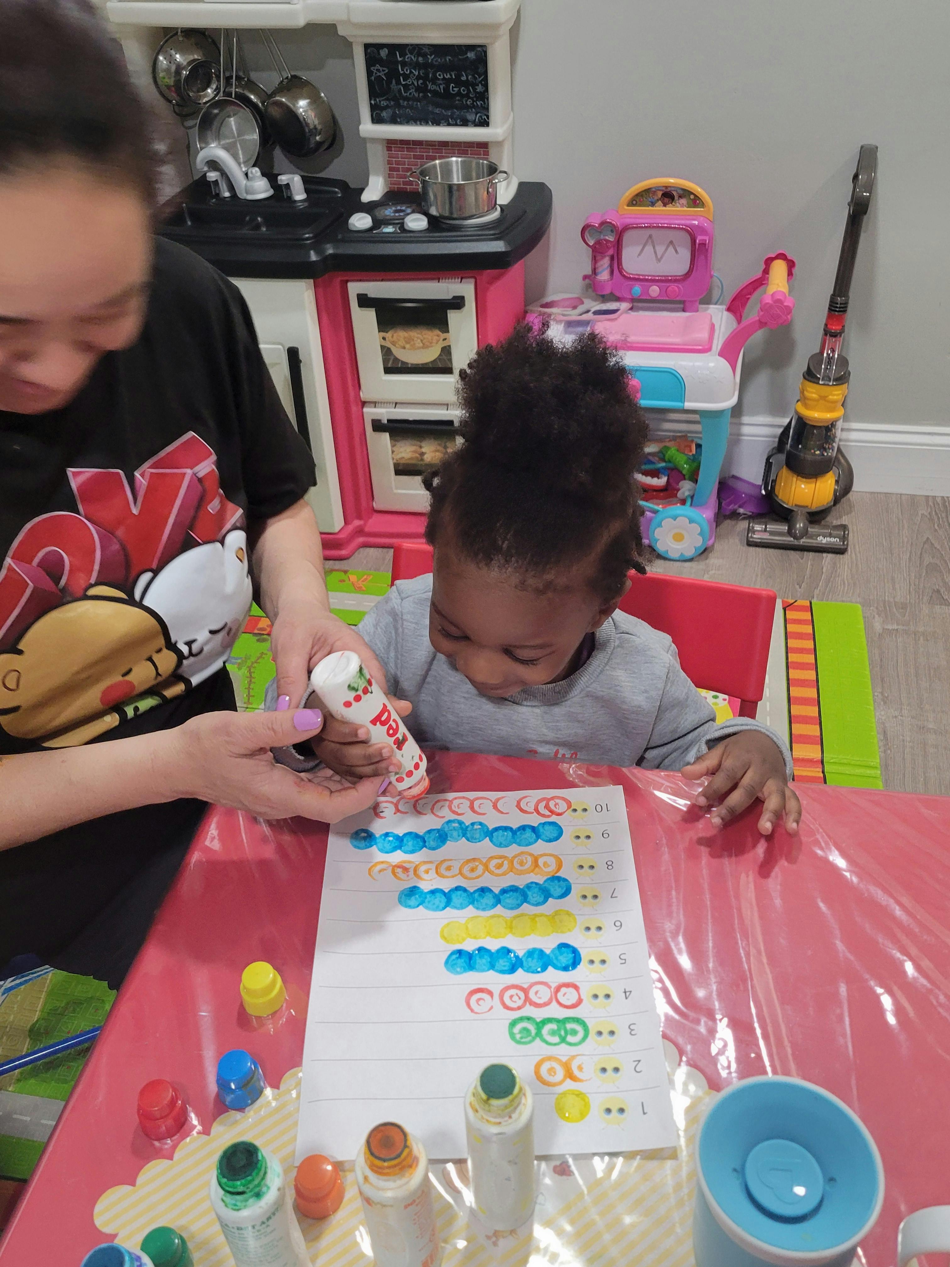 Person helping a child use a dot marker on a worksheet