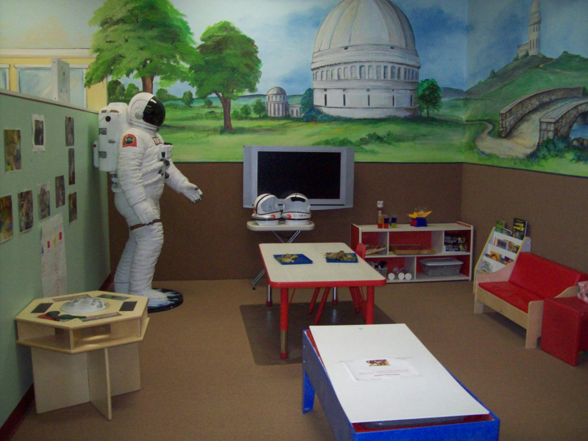 Astronaut figure in a room with tables, chairs, and a mural
