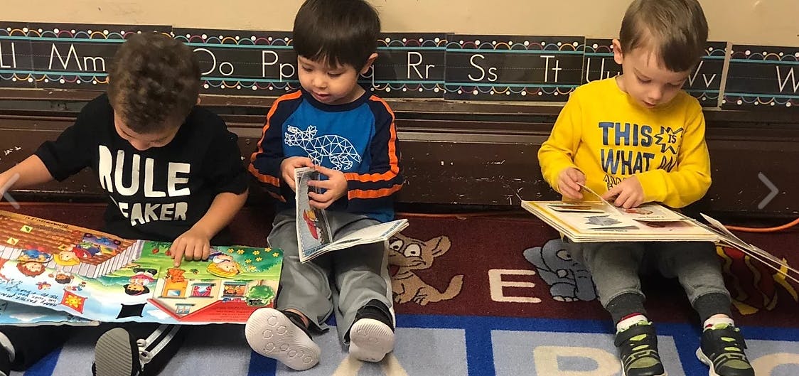 Three children sitting on a rug, reading books