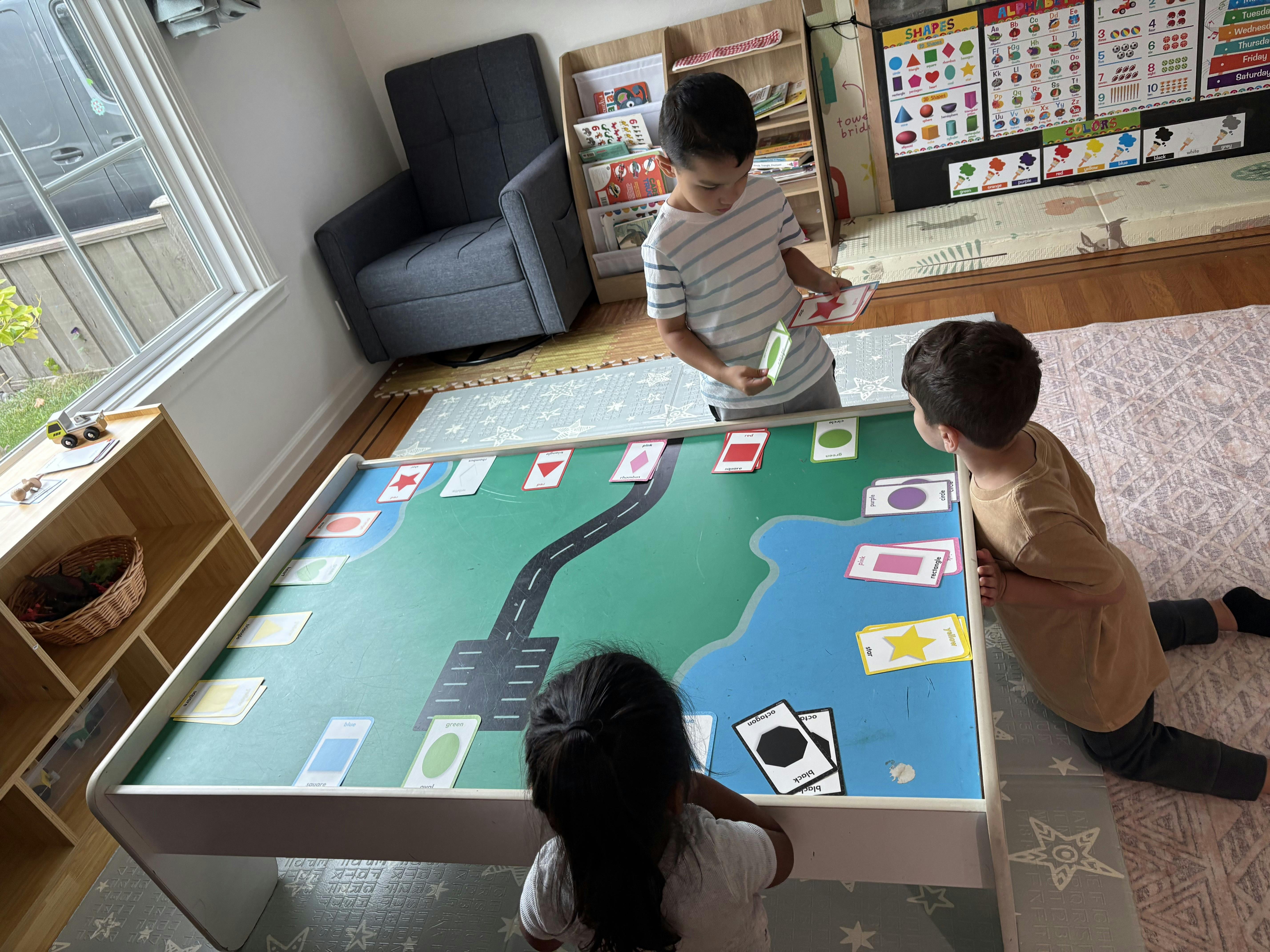 Three children playing around a table with a road and water mat