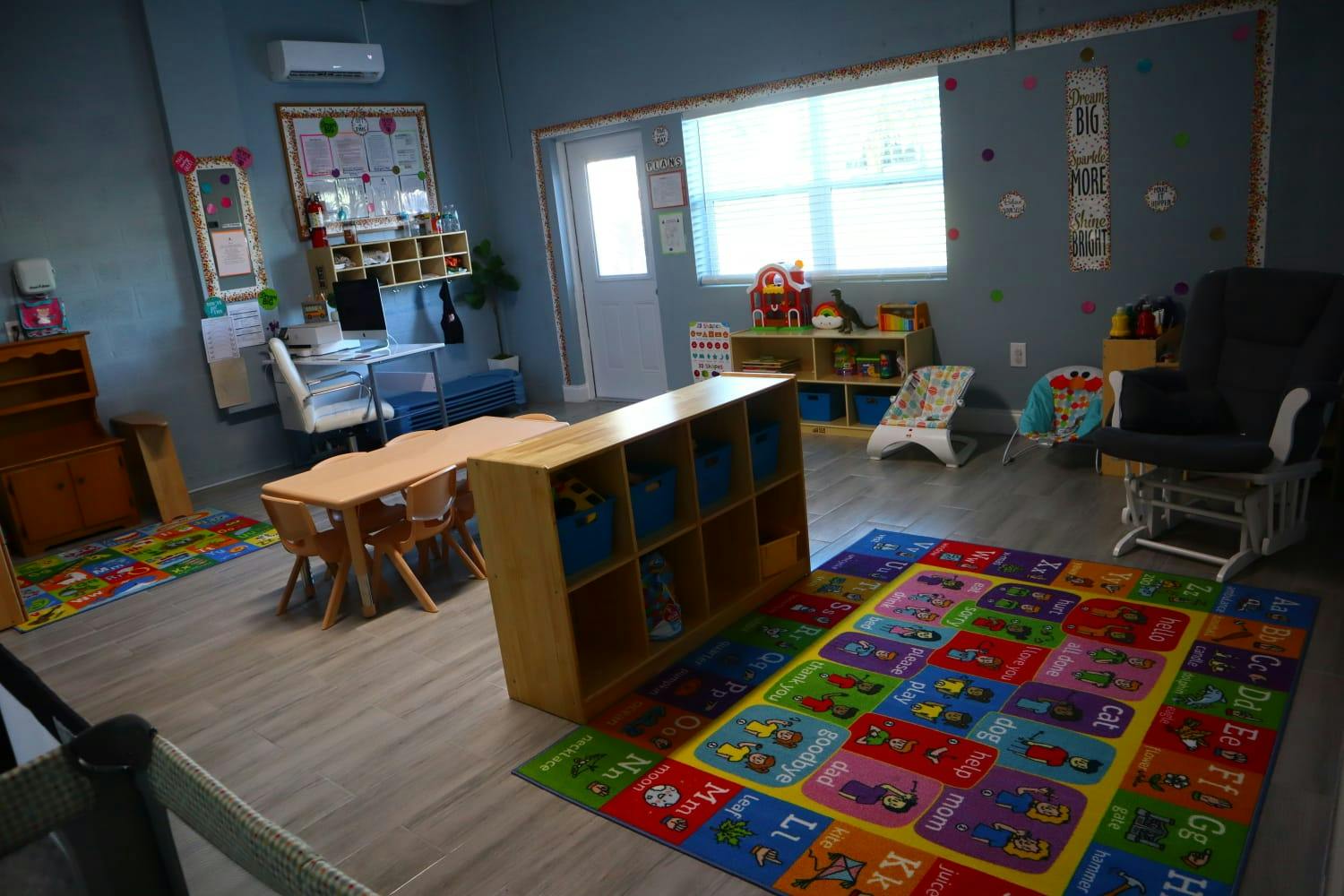 A classroom with small tables, chairs, storage units, and a colorful rug