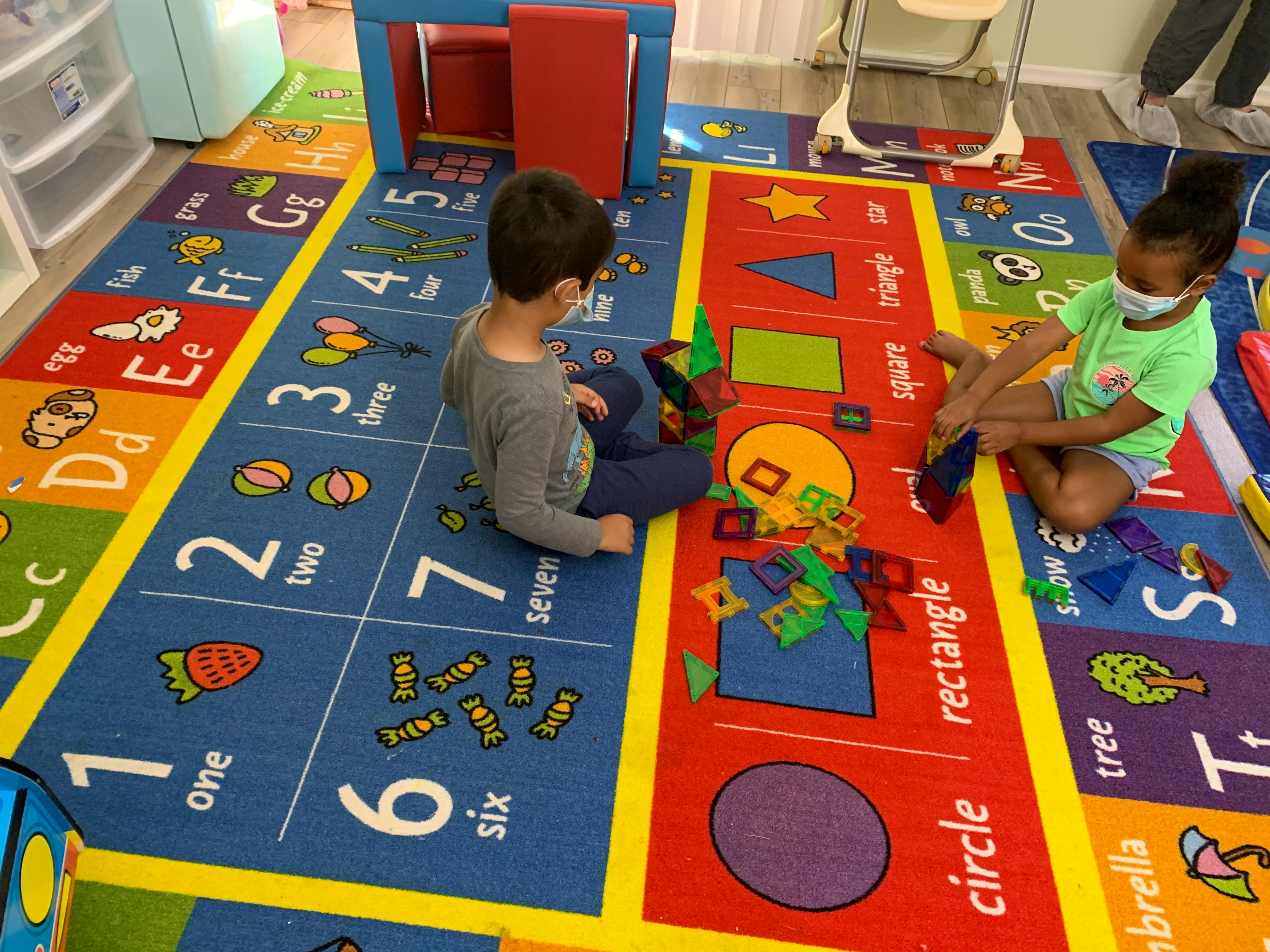 Two children playing with magnetic shapes on a colorful rug