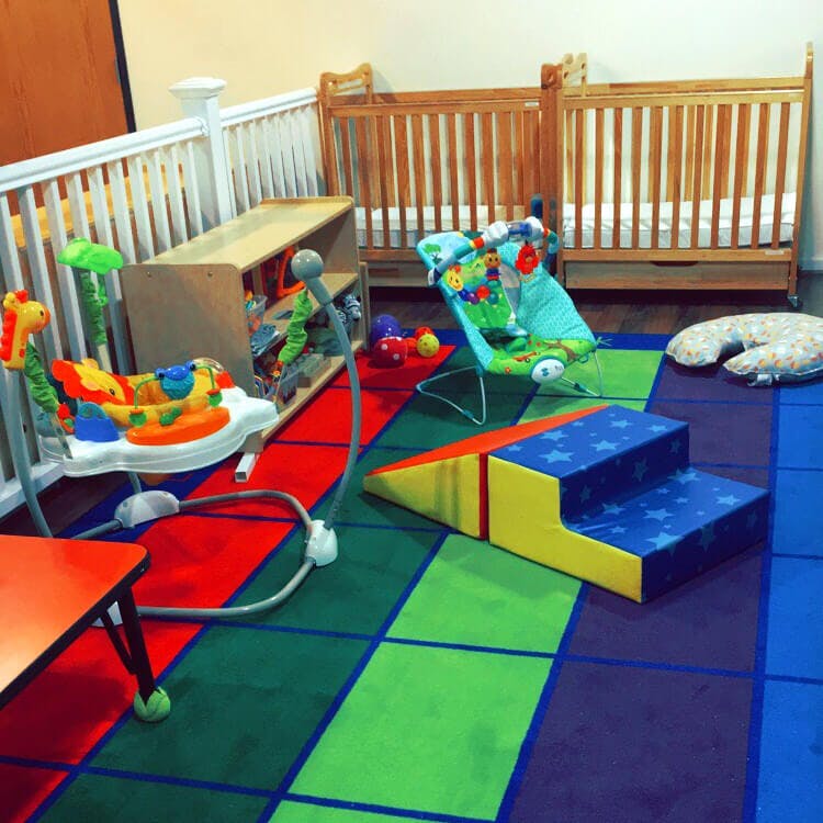 Two cribs and baby play equipment on a colorful floor