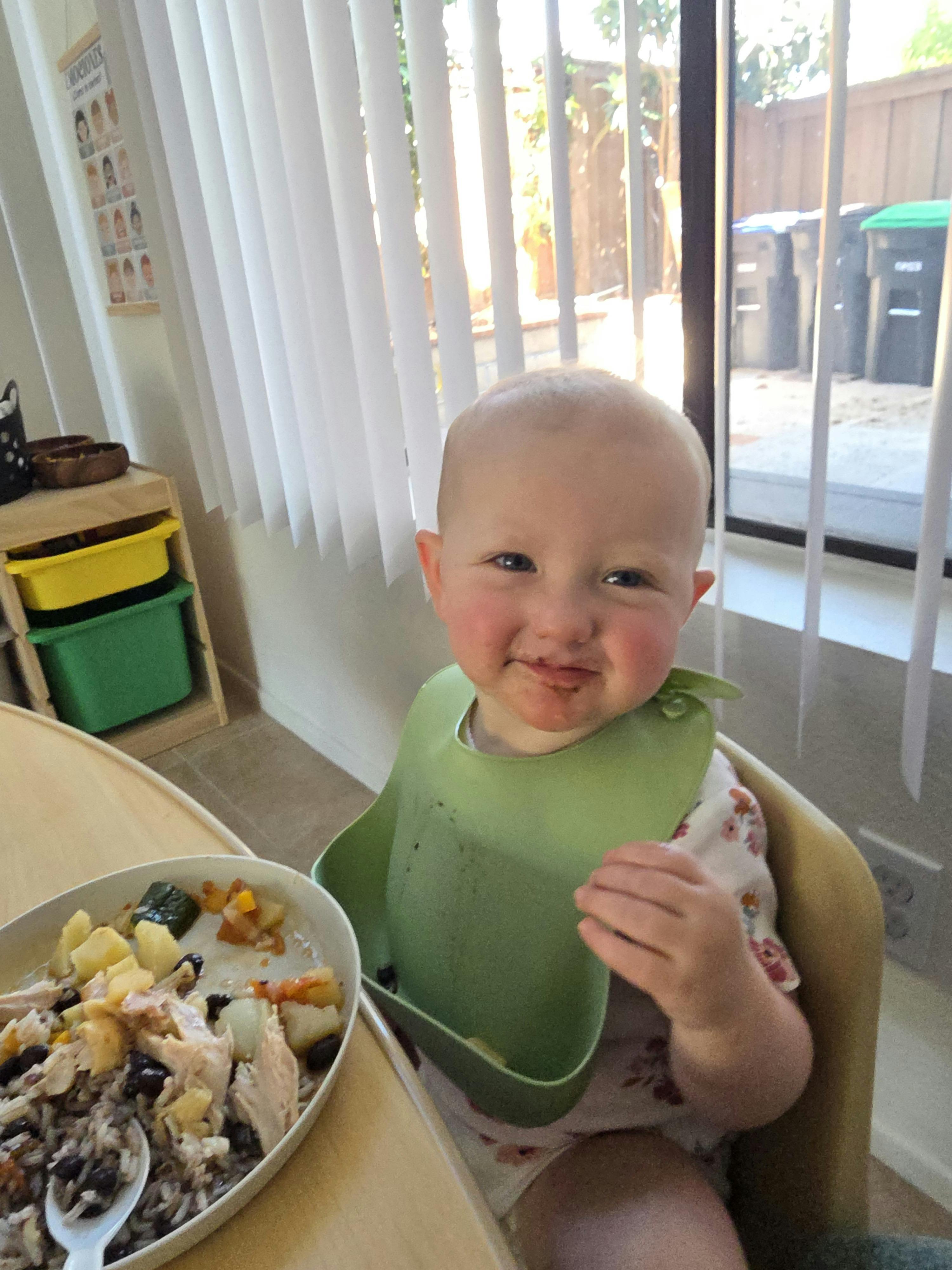 Child in high chair with food on face and bowl of plate