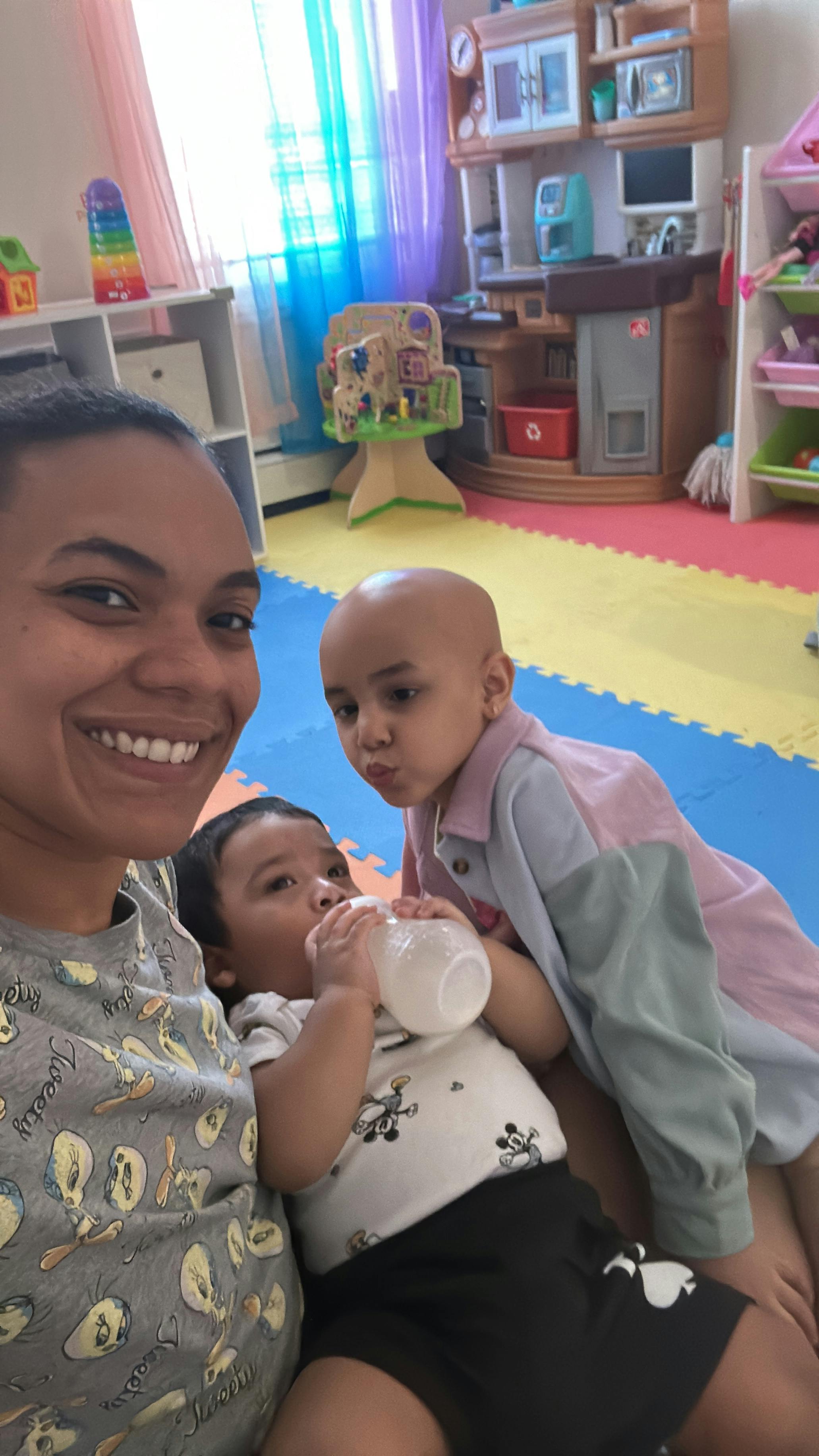Person smiling with two children, one drinking from a bottle