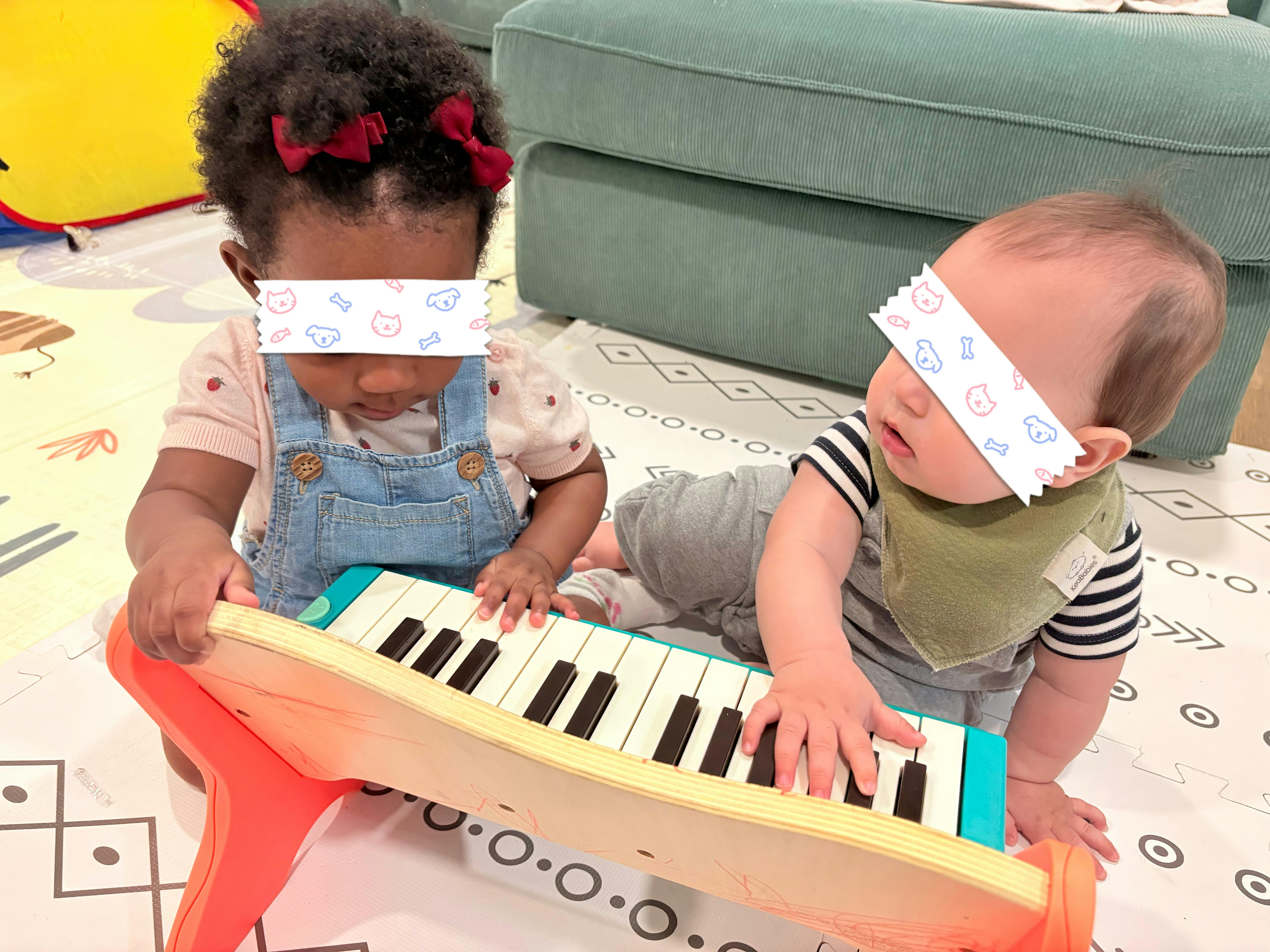 Two children playing with a toy piano on a play mat