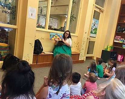 Person reading a book to a group of children sitting children