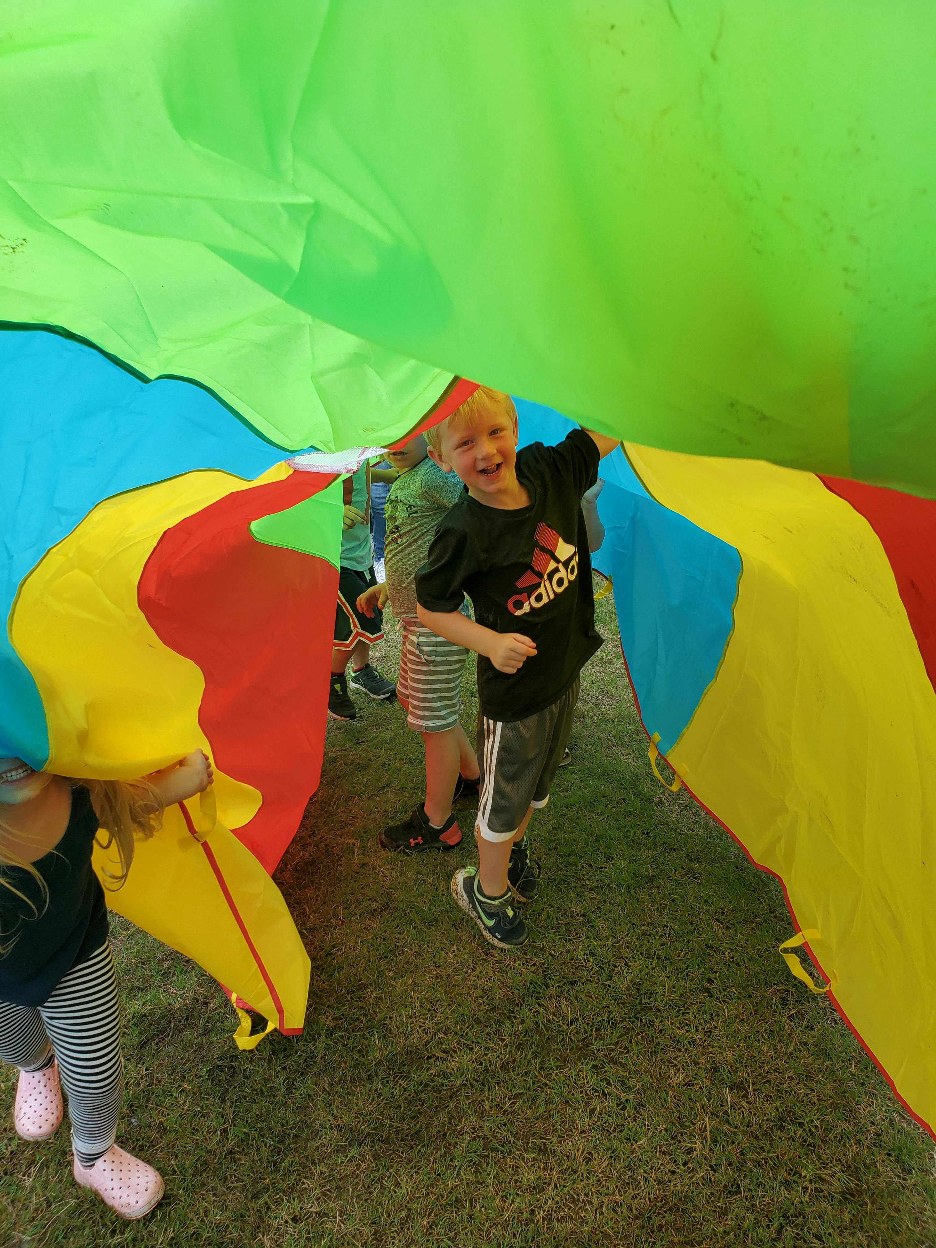 Child standing under a colorful parachute with other children
