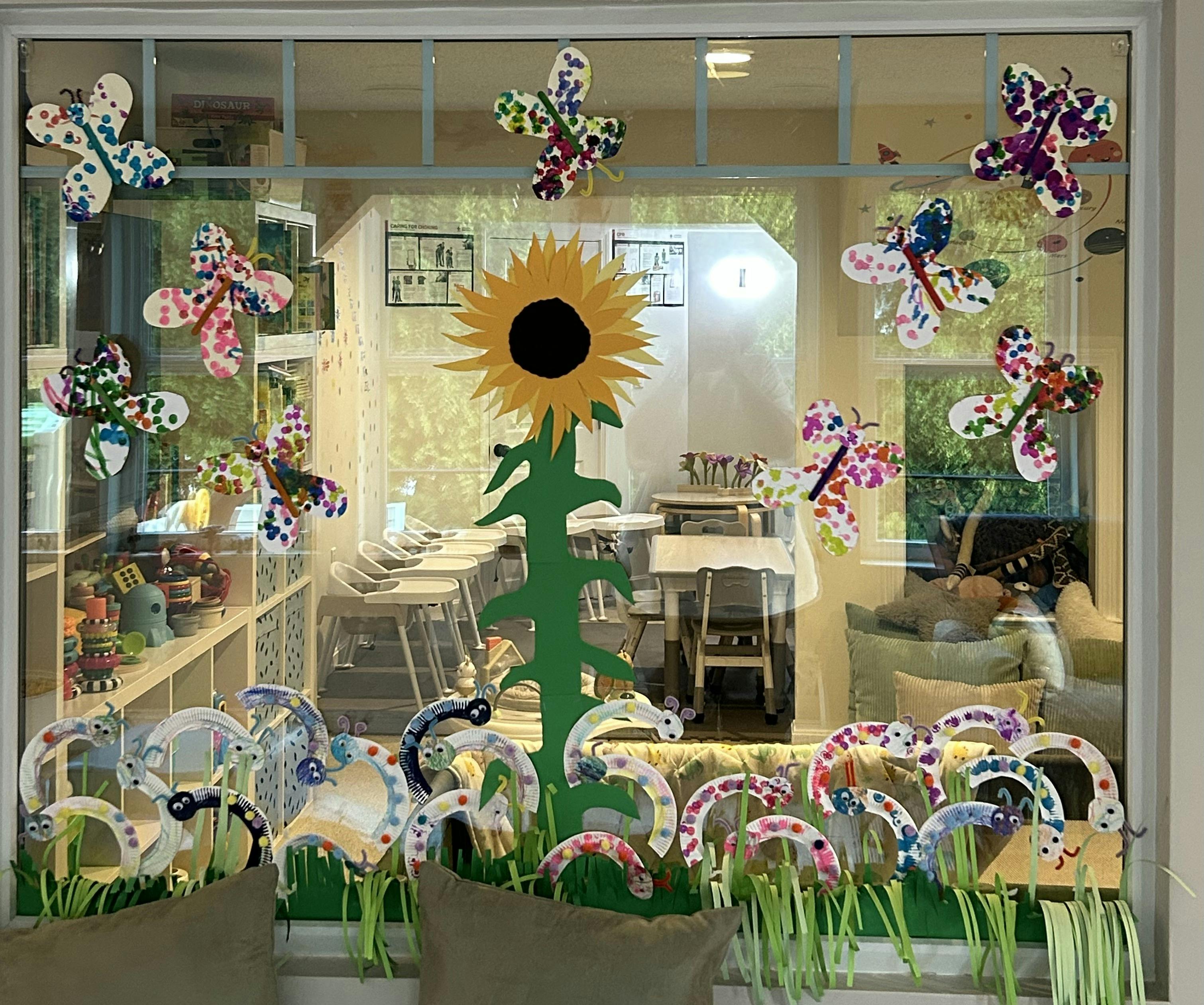 Window decorated with paper butterflies, a sunflower, and other crafts