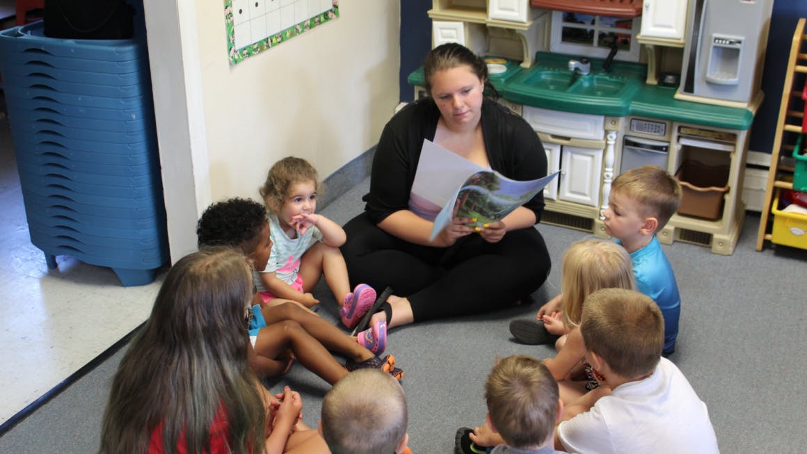 Person reading a book to a group of children in a classroom