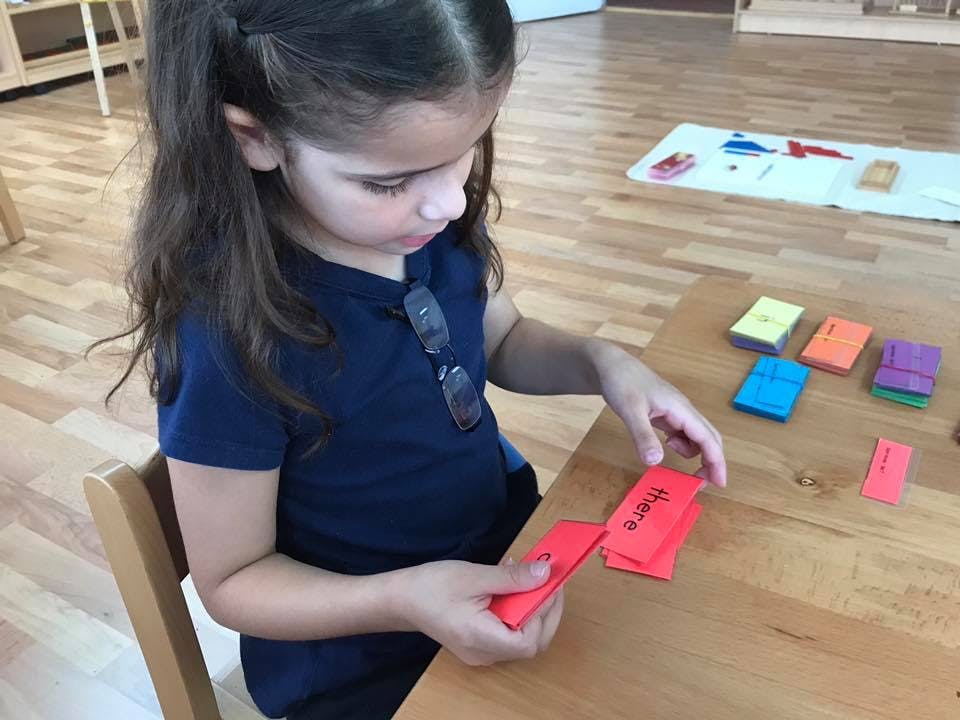 Child holding red cards with text on a wooden table