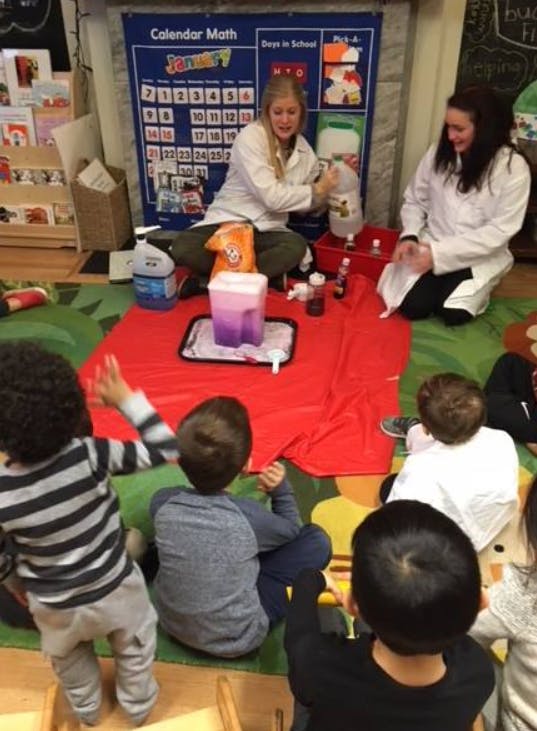 Two people in lab coats demonstrating a science experiment to children