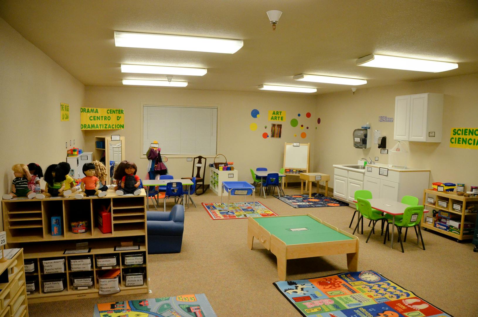 A classroom with small tables, chairs, and shelves with toys