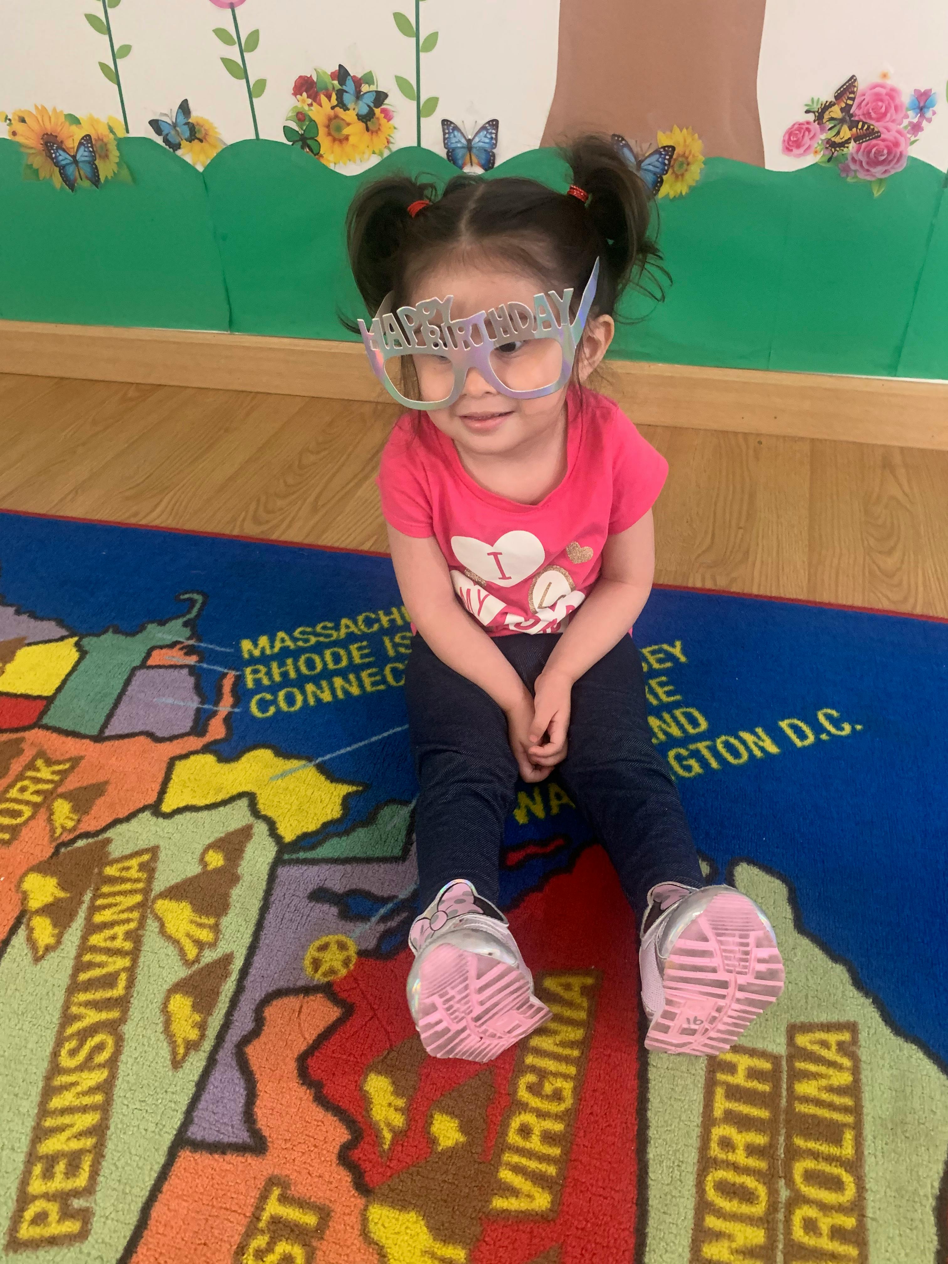 Child wearing birthday glasses sitting on a map rug
