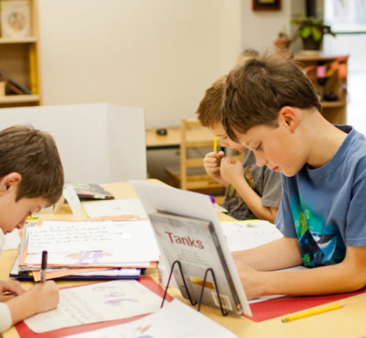 Children writing and reading at desks in a classroom