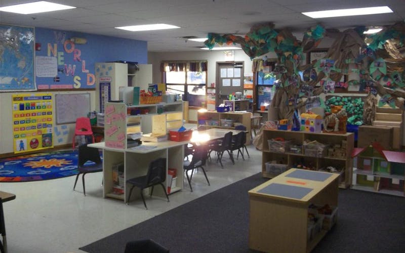 An empty classroom with desks, chairs, storage units, and a large tree decoration