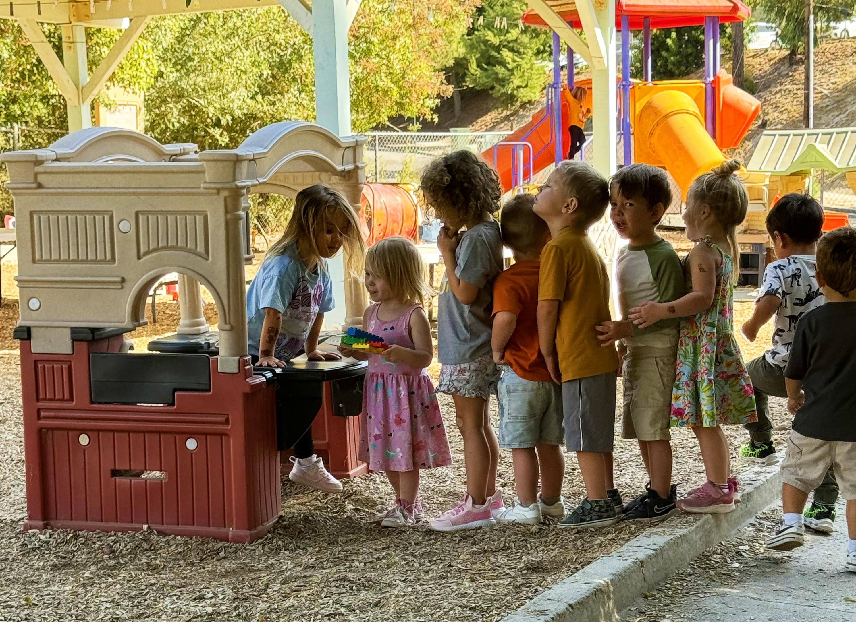 Group of children playing near a plastic play kitchen at a park