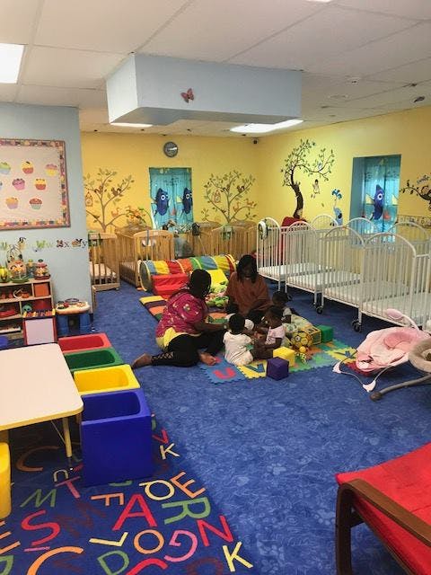 Two people and multiple children playing on a mat in a daycare room