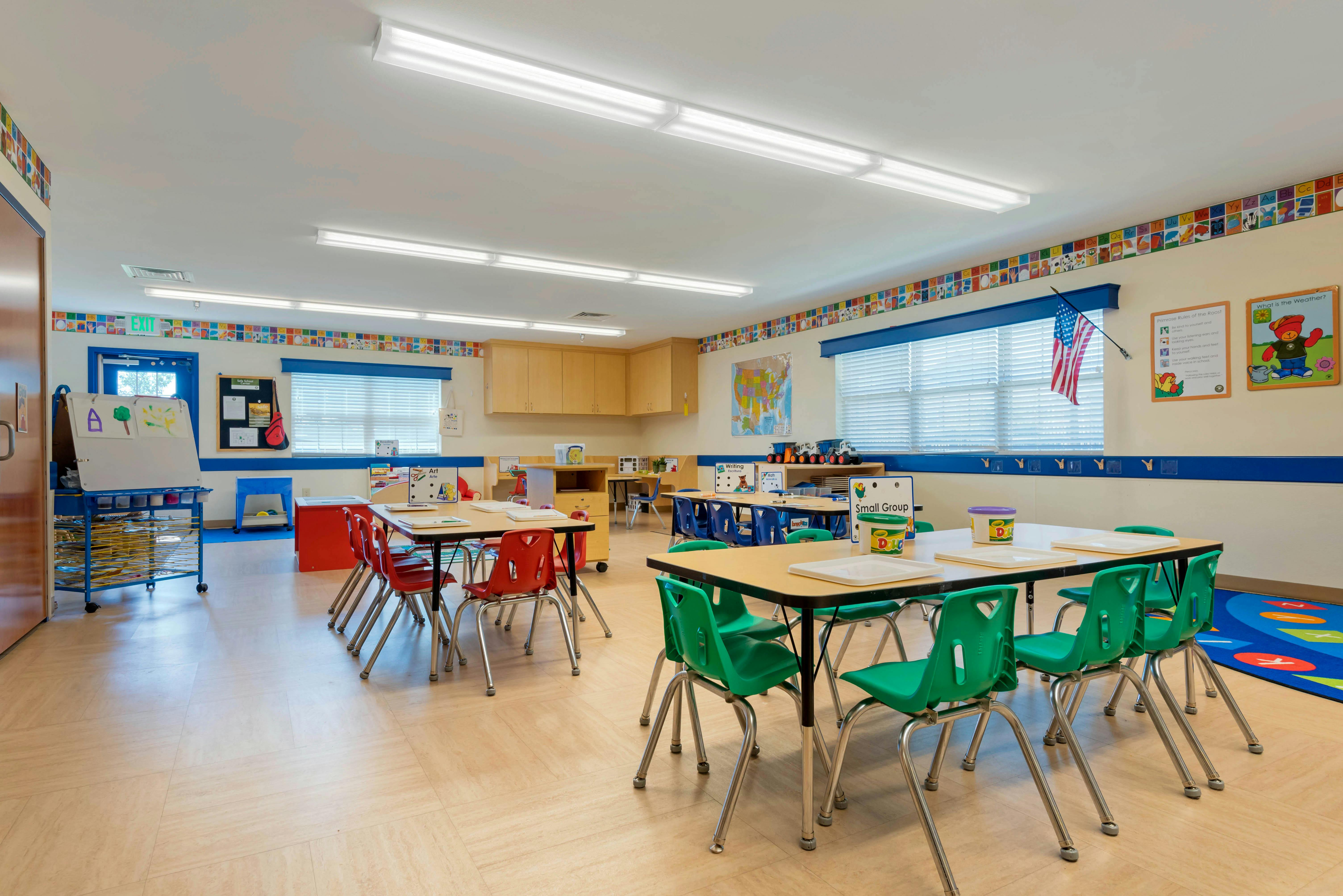 Empty classroom with small tables and chairs, art drying rack, bulletin board, small group sign