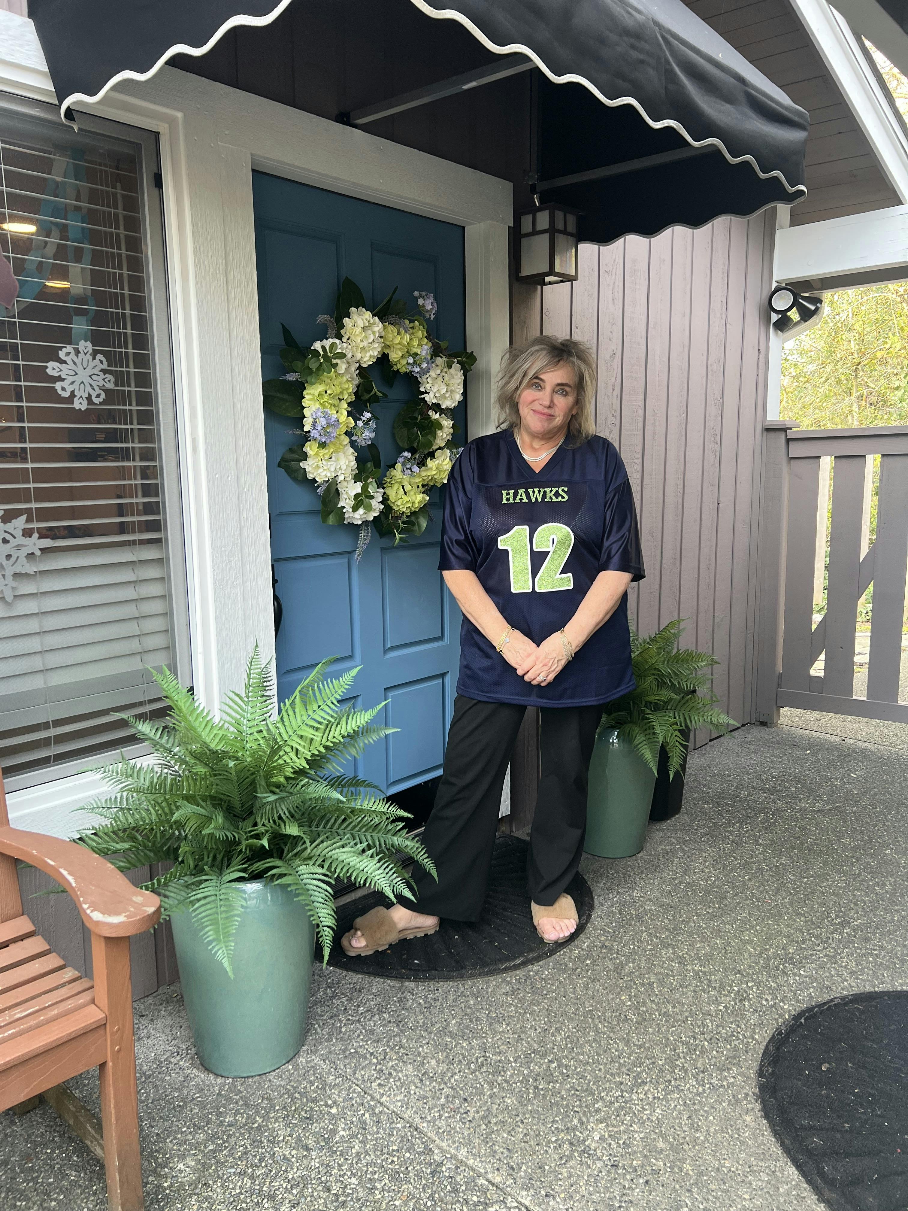Person in a dark blue jersey with "HAWKS 12" in green standing by a door