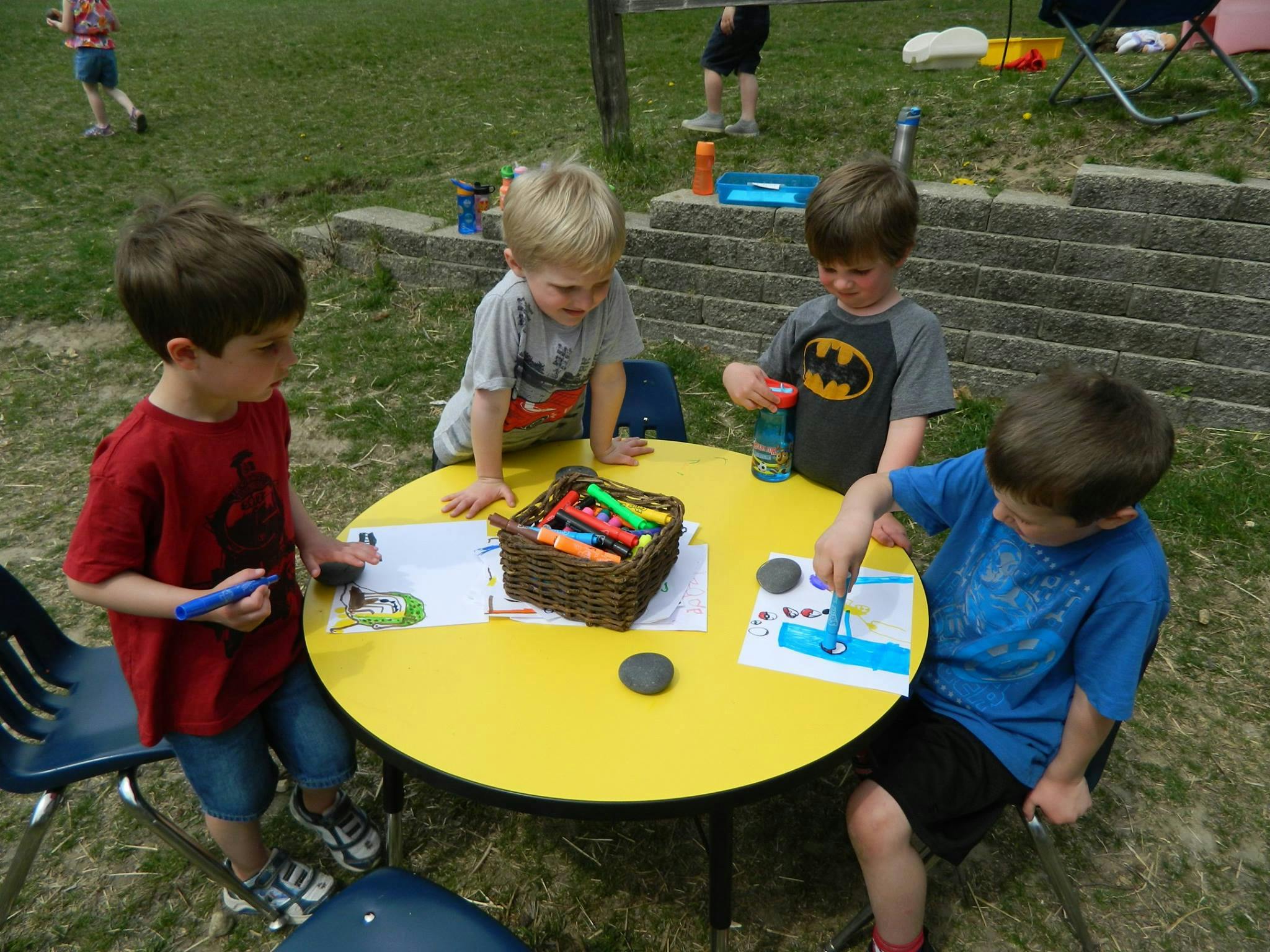 Four children drawing and coloring at a yellow table outdoors