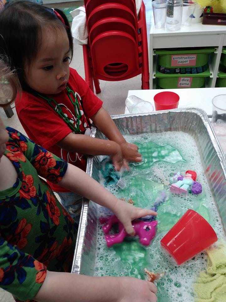 Two children playing with toys in a tray of soapy water