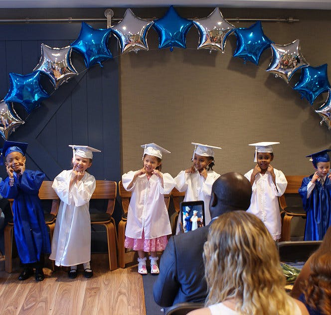 Children in graduation caps and gowns posing under star balloons