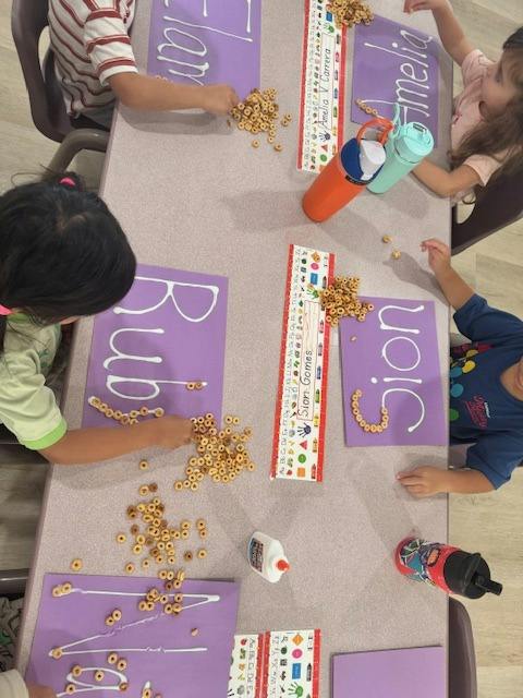 Children arranging cereal loops on paper with names written in glue