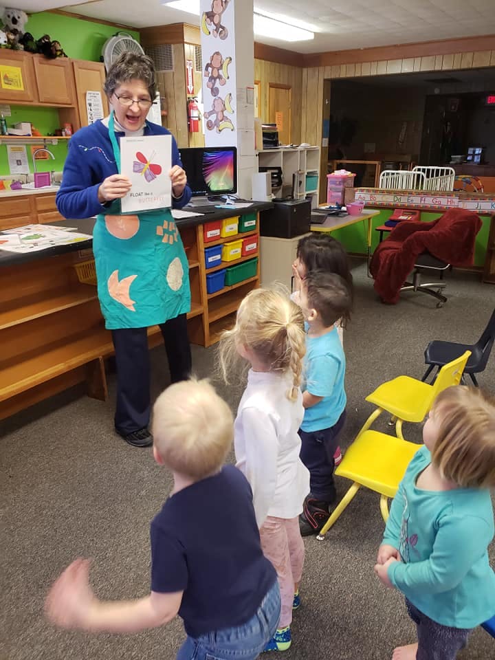 Person holding up a drawing for a group of children in a classroom